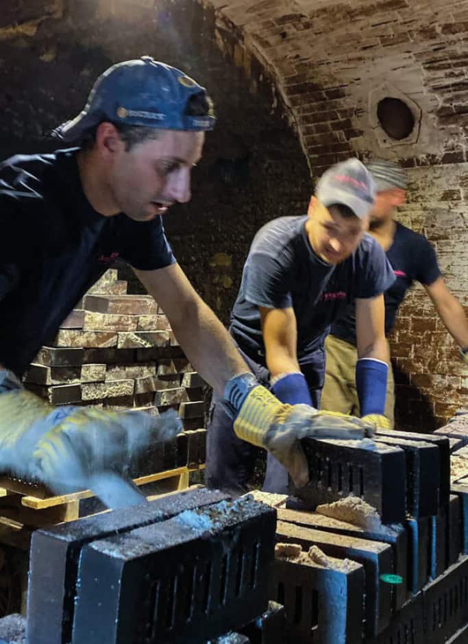 Zwei Männer bei der Arbeit im Ringofen, die mit Handschuhen Klinker aufschichten